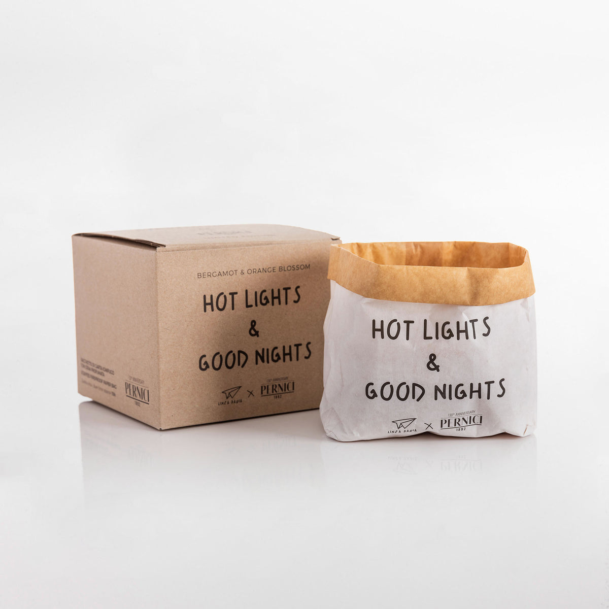 Candela profumata in sacchetto di carta con la scritta “Hot lights & Good Nights”, fotografata in still life, fragranza Bergamot & Orange